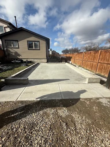 Residential house with concrete driveway, wooden fence, and blue cloudy sky