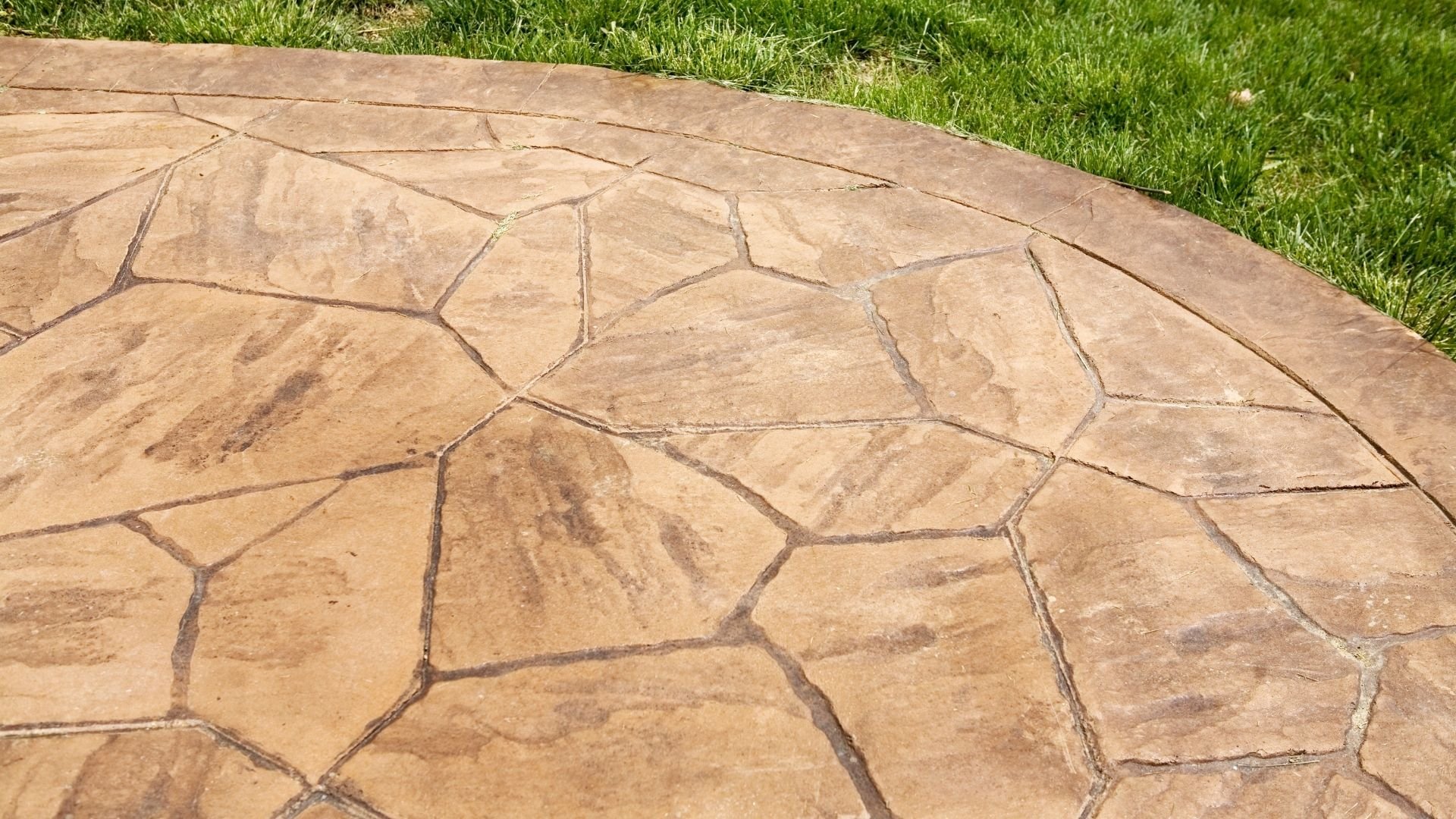 Close-up of tan flagstone patio with irregular shapes and green grass border
