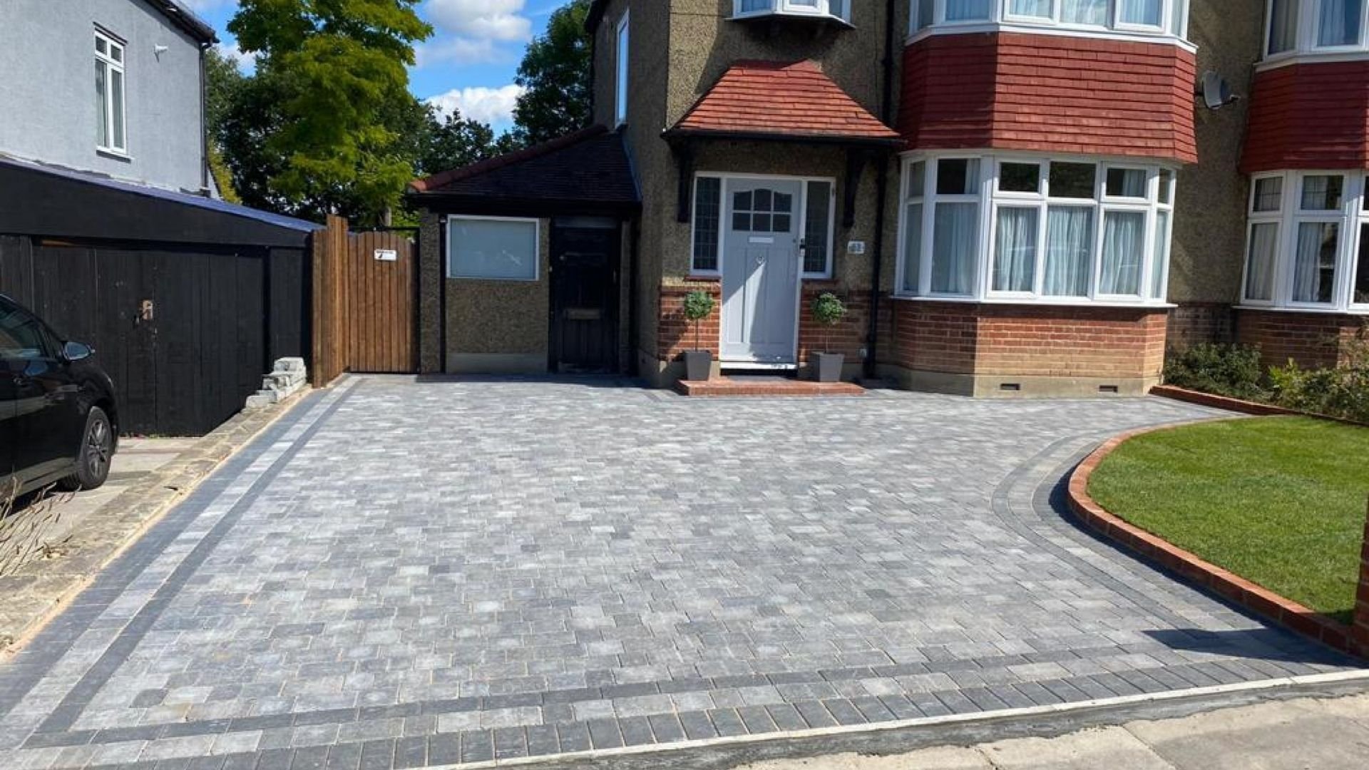 Modern paved driveway with brick edging in front of residential homes with red tile roofs.