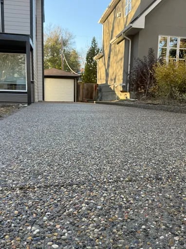 Modern house with gravel driveway, yellow exterior wall, and evergreen trees nearby.