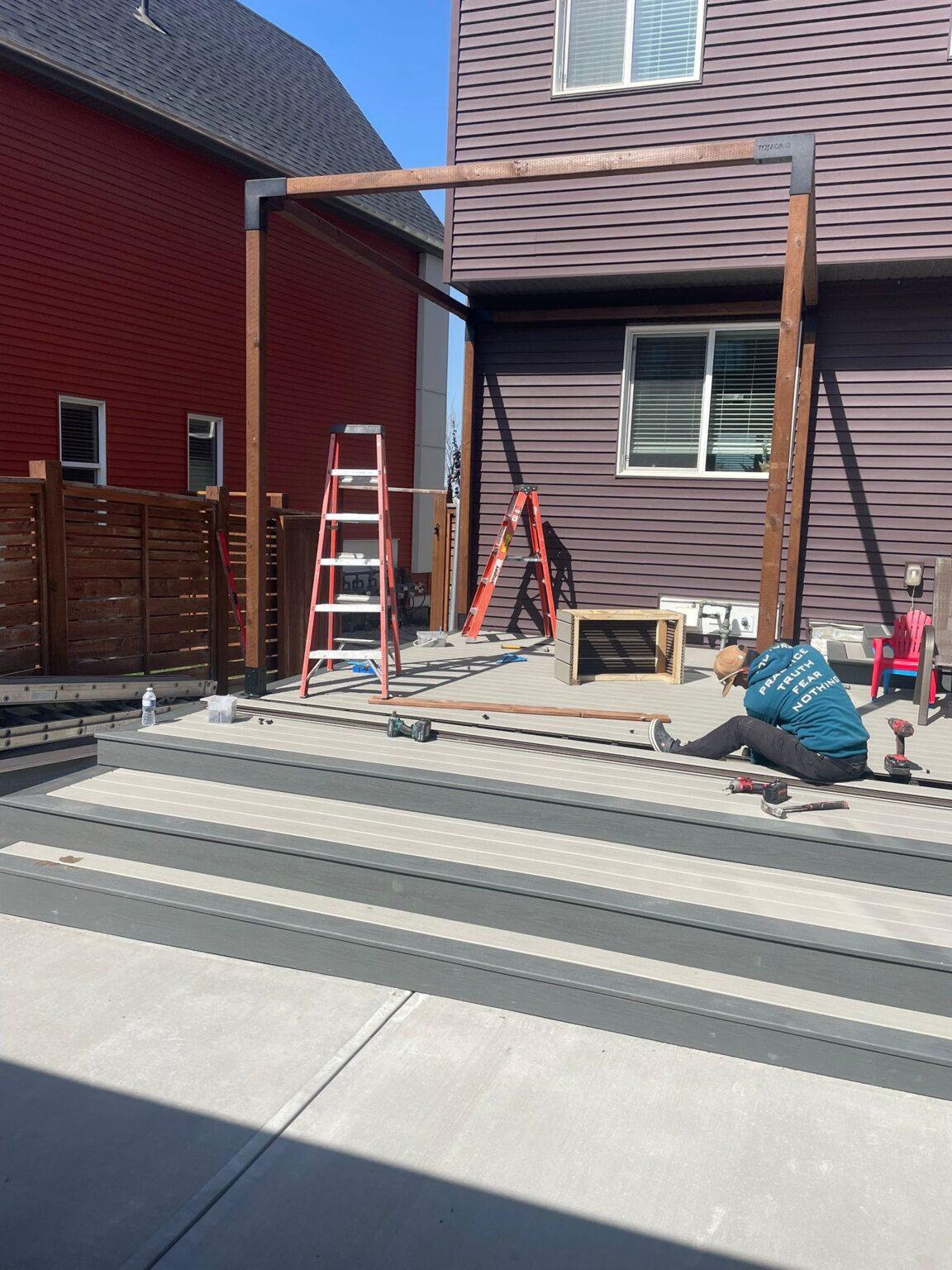 Construction worker installing decking on residential house patio with wooden pergola and ladders