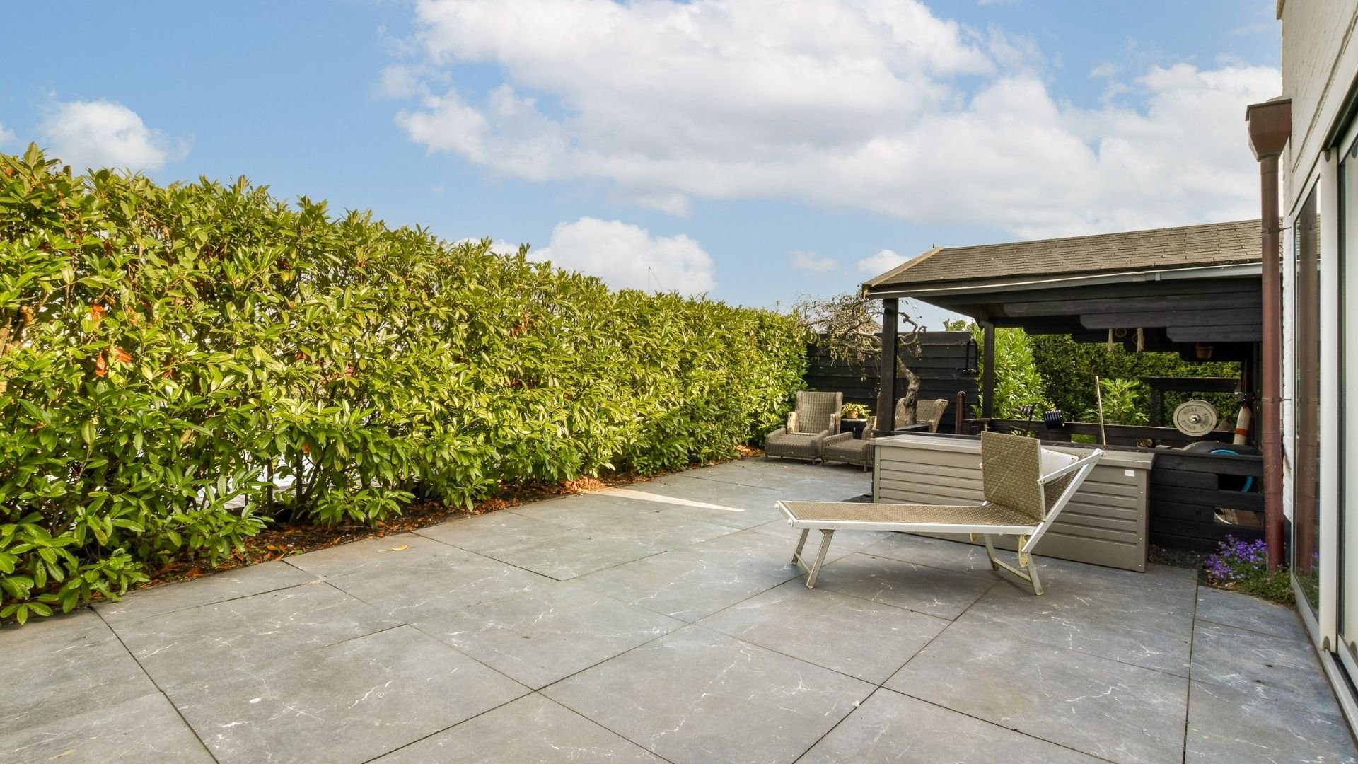 Patio with lounge chairs, pergola, and lush green hedge under blue sky
