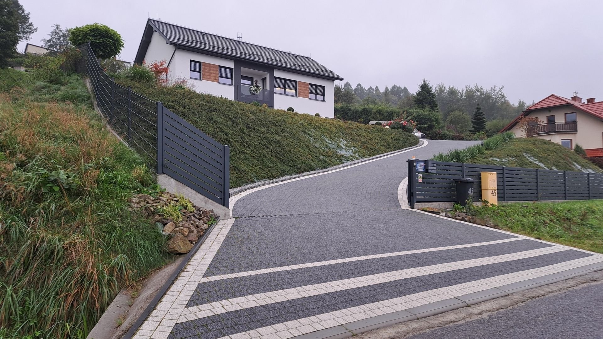 Modern residential driveway with striped paving leading to contemporary hilltop house with metal gates
